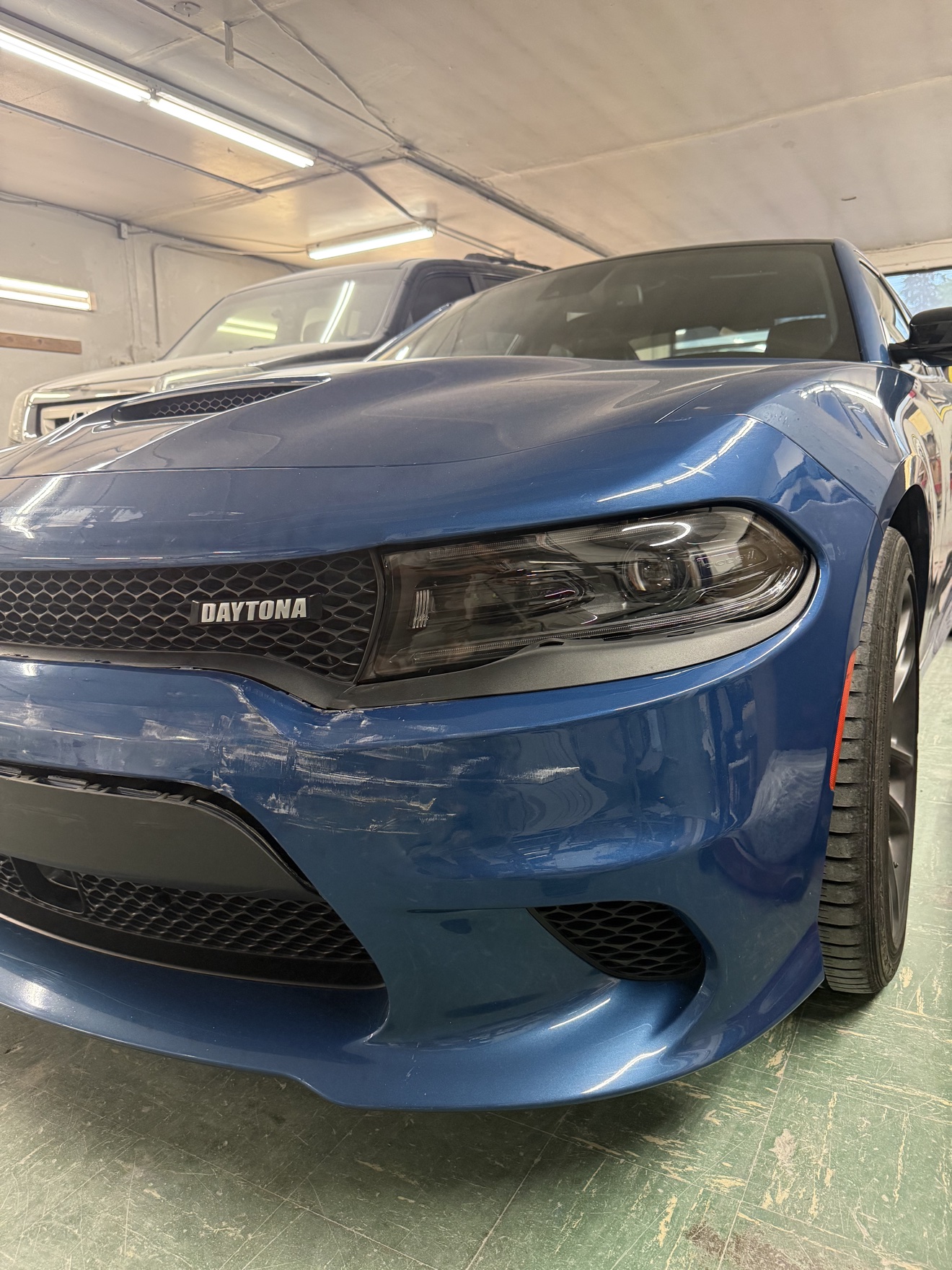 Blue Dodge Charger front bumper with scuffs before repair / Defensa delantera de un Dodge Charger azul con raspaduras antes de la reparación