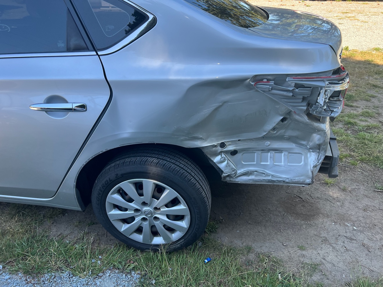 Silver Nissan Sentra with severe rear quarter panel and taillight damage before repair / Nissan Sentra plateado con daños graves en el panel lateral trasero y la luz trasera antes de la reparación