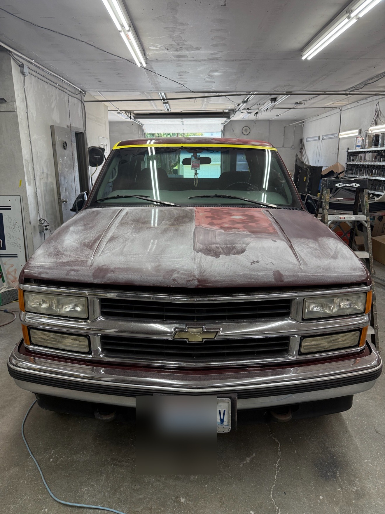 Front view of a Chevrolet pickup in the garage with a faded, sanded hood before refinishing / Vista frontal de una camioneta Chevrolet en el taller con el cofre desteñido y lijado antes del repintado
