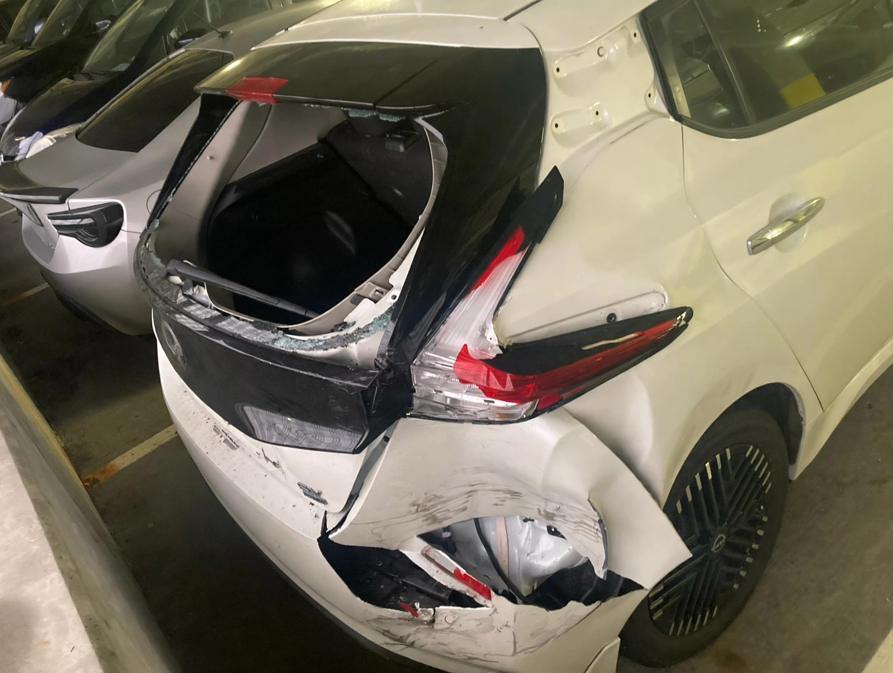 White Nissan Leaf with severe rear hatch, taillight, quarter panel, and bumper damage before repair / Nissan Leaf blanco con daños graves en la compuerta, la luz trasera, el panel lateral y la defensa antes de la reparación